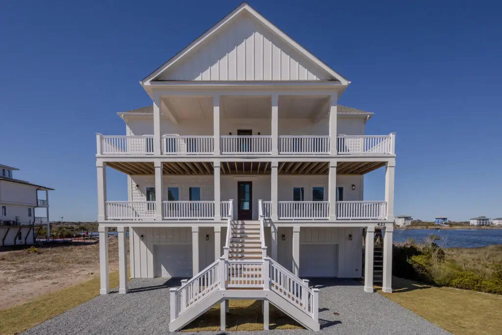 Three-story coastal home with board and batten siding, double porches, symmetrical gables, and elevated entry staircase.