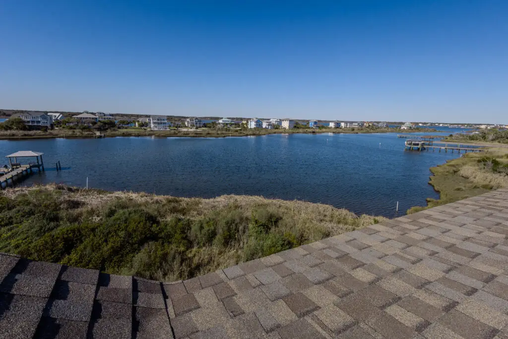 Scenic soundfront view with calm water, marsh grasses, docks, and coastal homes under a clear blue sky.