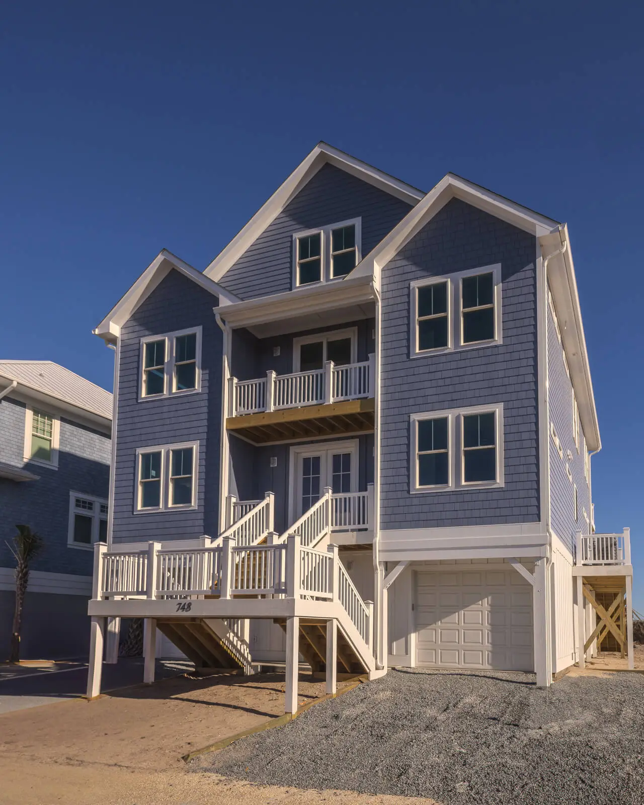 Three-story coastal home with blue shake siding, white trim, double front porches, and elevated entry with garage below.